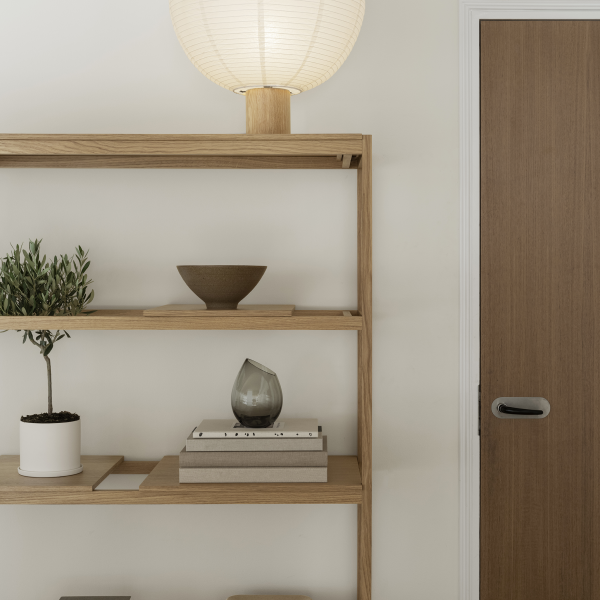 Modern wooden bookshelf with decorative items and a stylish lamp beside a door.