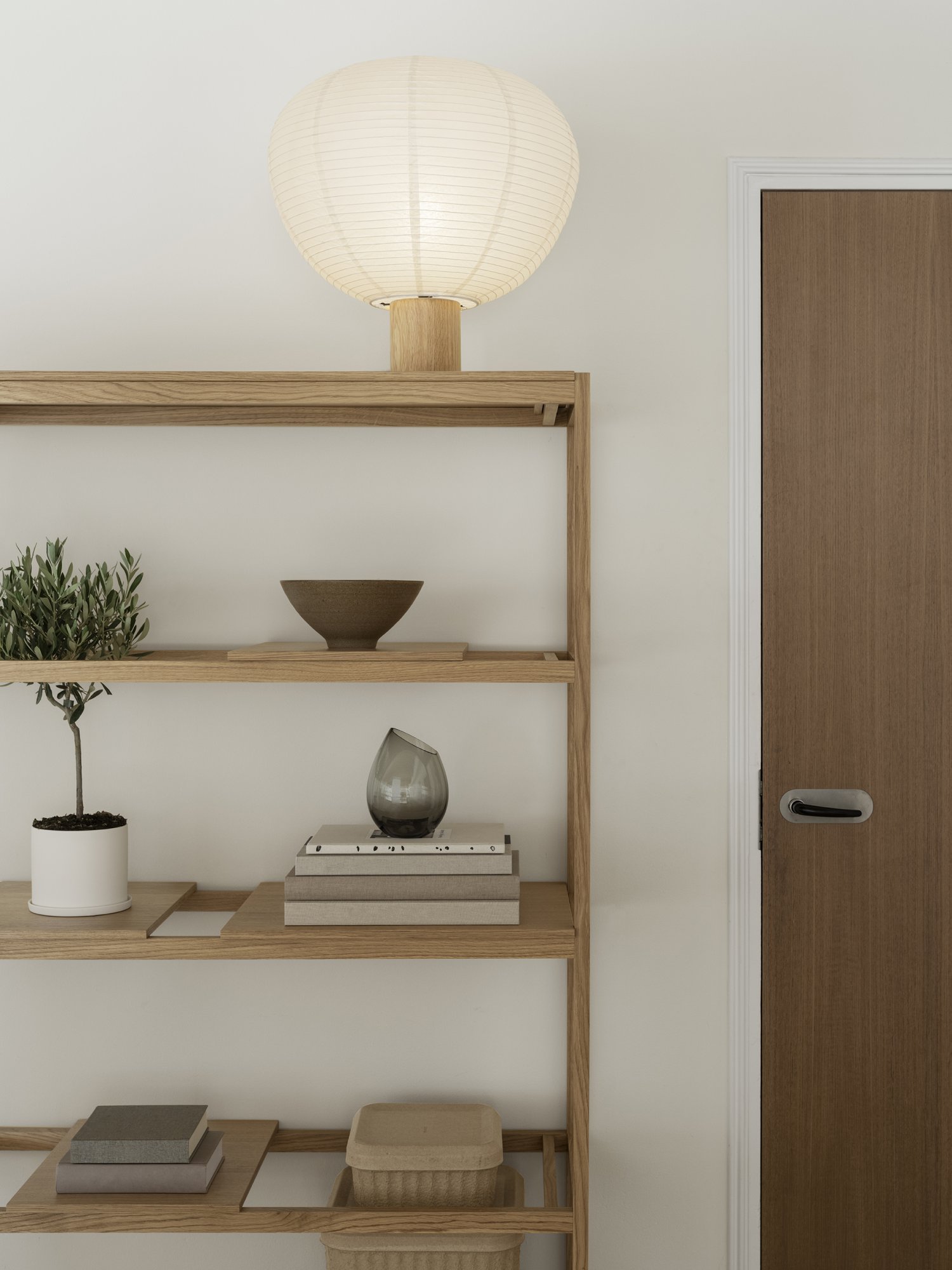 Modern wooden bookshelf with decorative items and a stylish lamp beside a door.