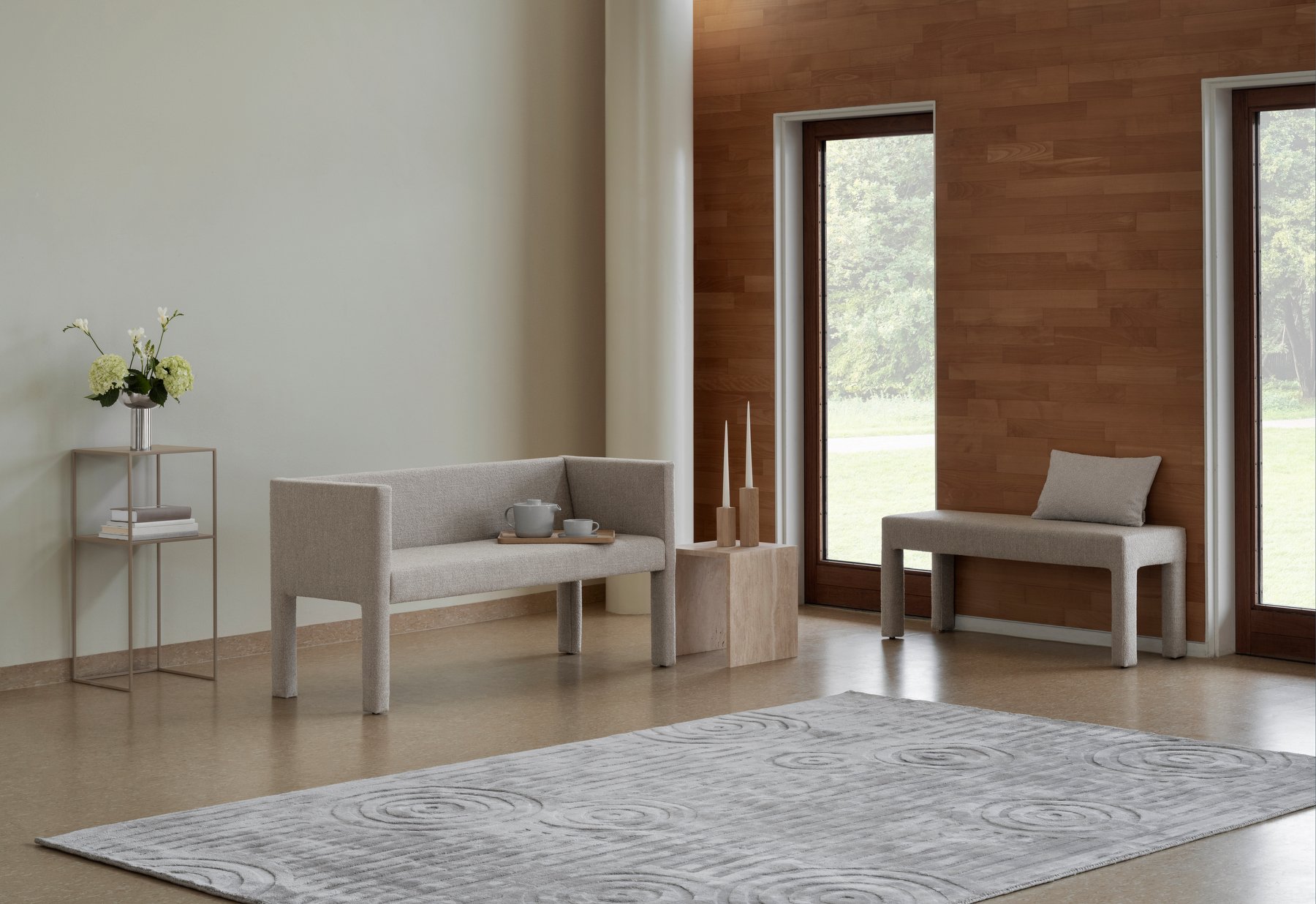 Modern living room with minimalist gray furniture, wooden accents, and a soft area rug.