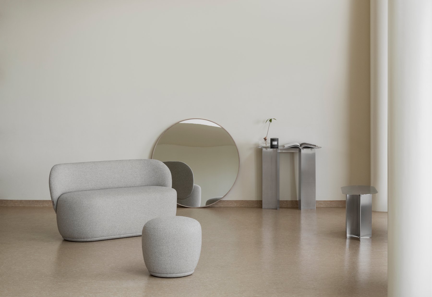 Modern living room featuring a gray sofa, round mirror, and sleek metallic furniture.