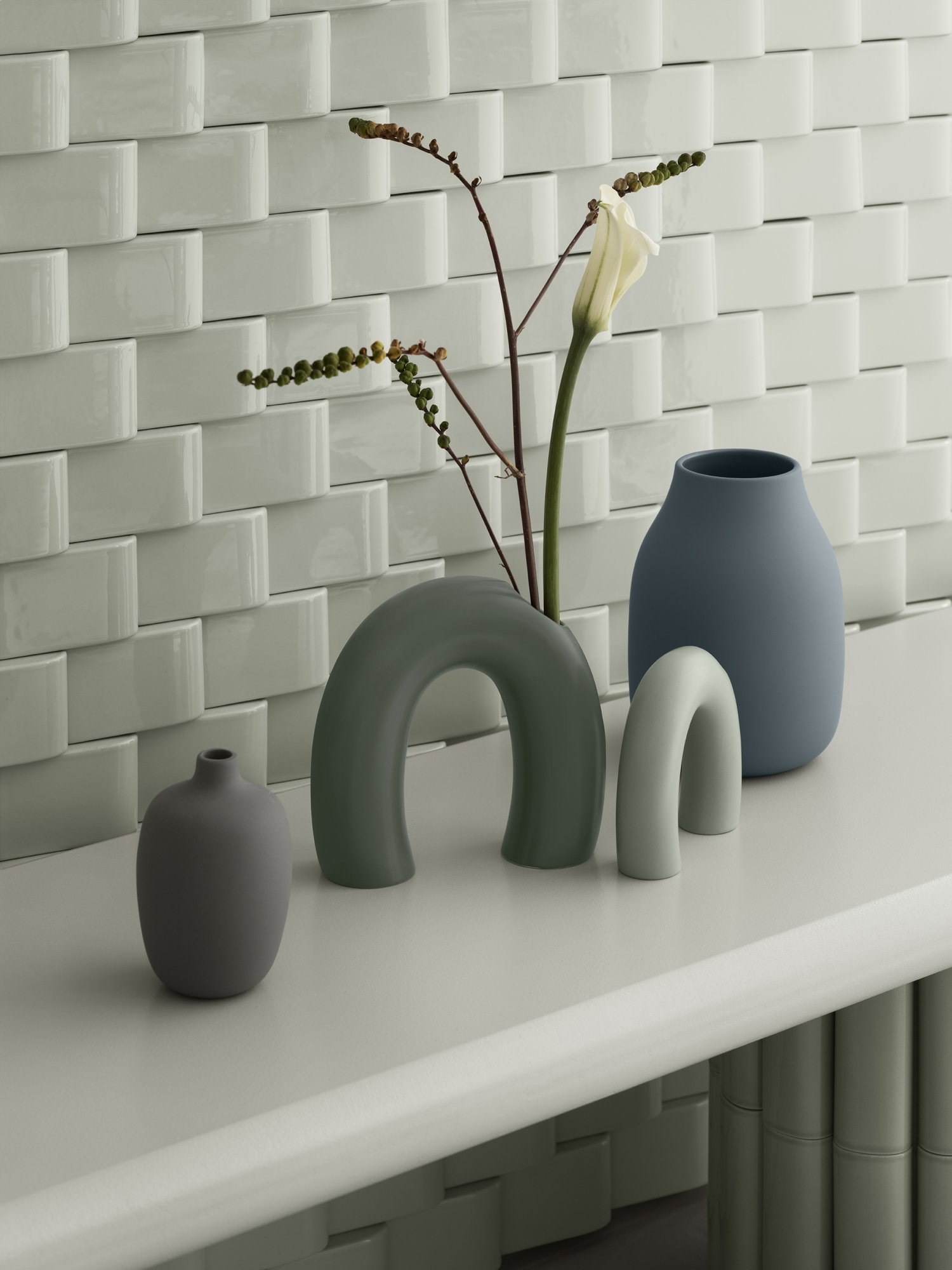 Decorative ceramic vases in soft colors displayed against a textured tile background.