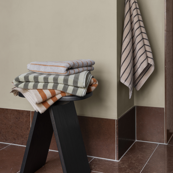 Stacked striped towels in neutral tones on a black stool against a muted wall.