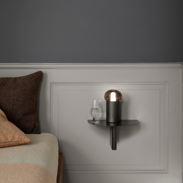 Stylish black wall lamp beside a glass on a minimalist bedside shelf.