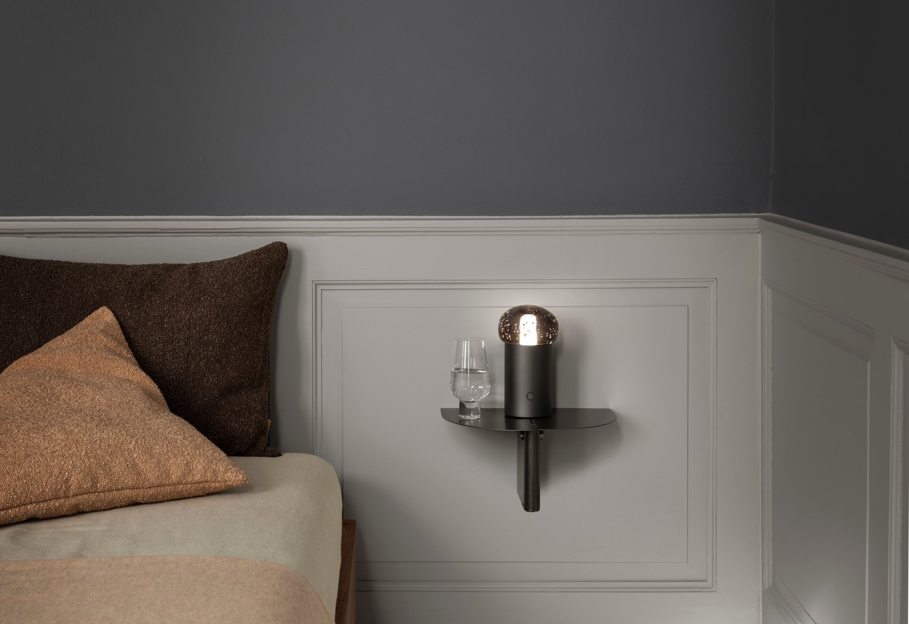 Stylish black wall lamp beside a glass on a minimalist bedside shelf.