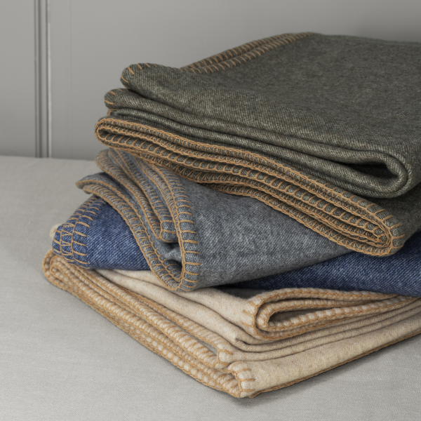 Cozy stacked blankets in various colors with decorative stitching on a soft surface.