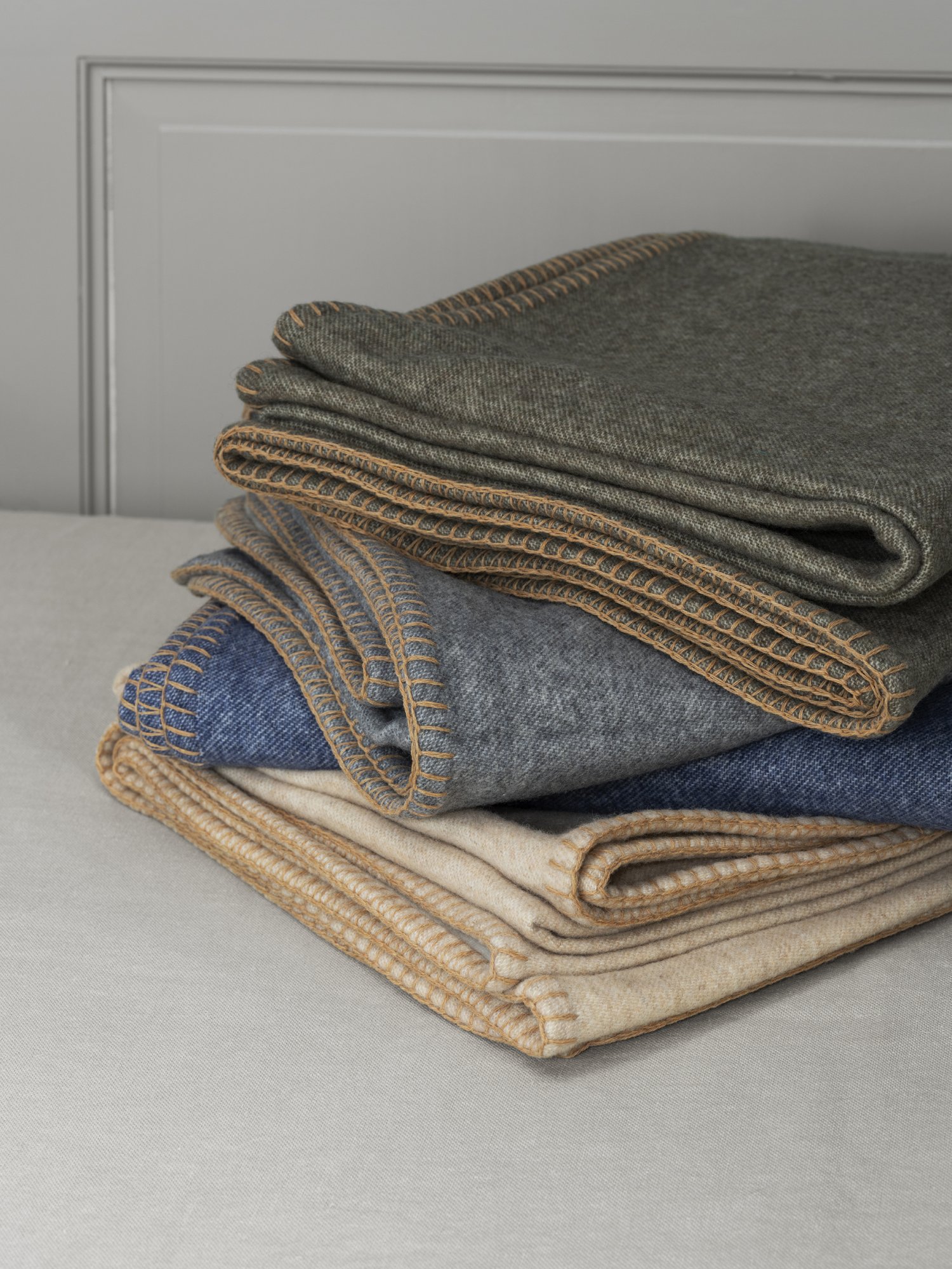 Cozy stacked blankets in various colors with decorative stitching on a soft surface.