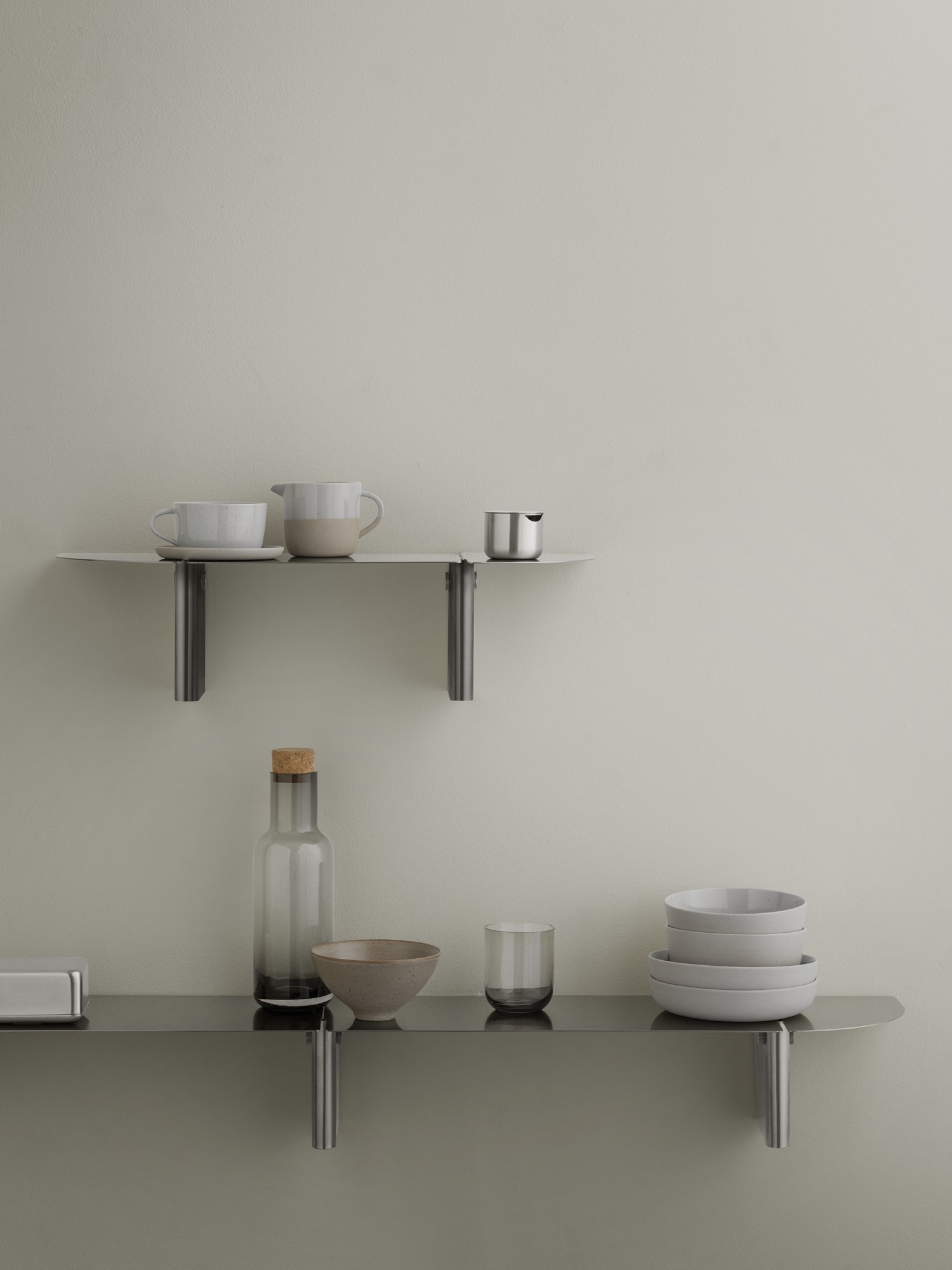 Minimalist kitchen shelf with modern ceramics and glassware against a neutral wall.