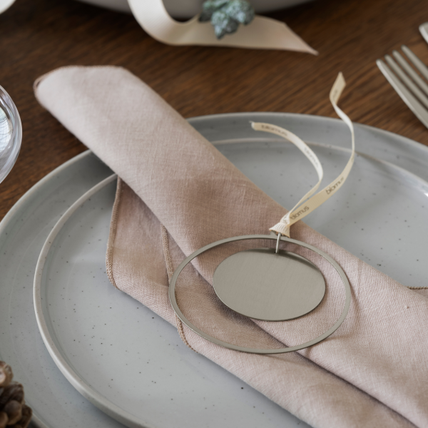 Stylish table setting with a beige napkin, metal tag, and rustic dishware.