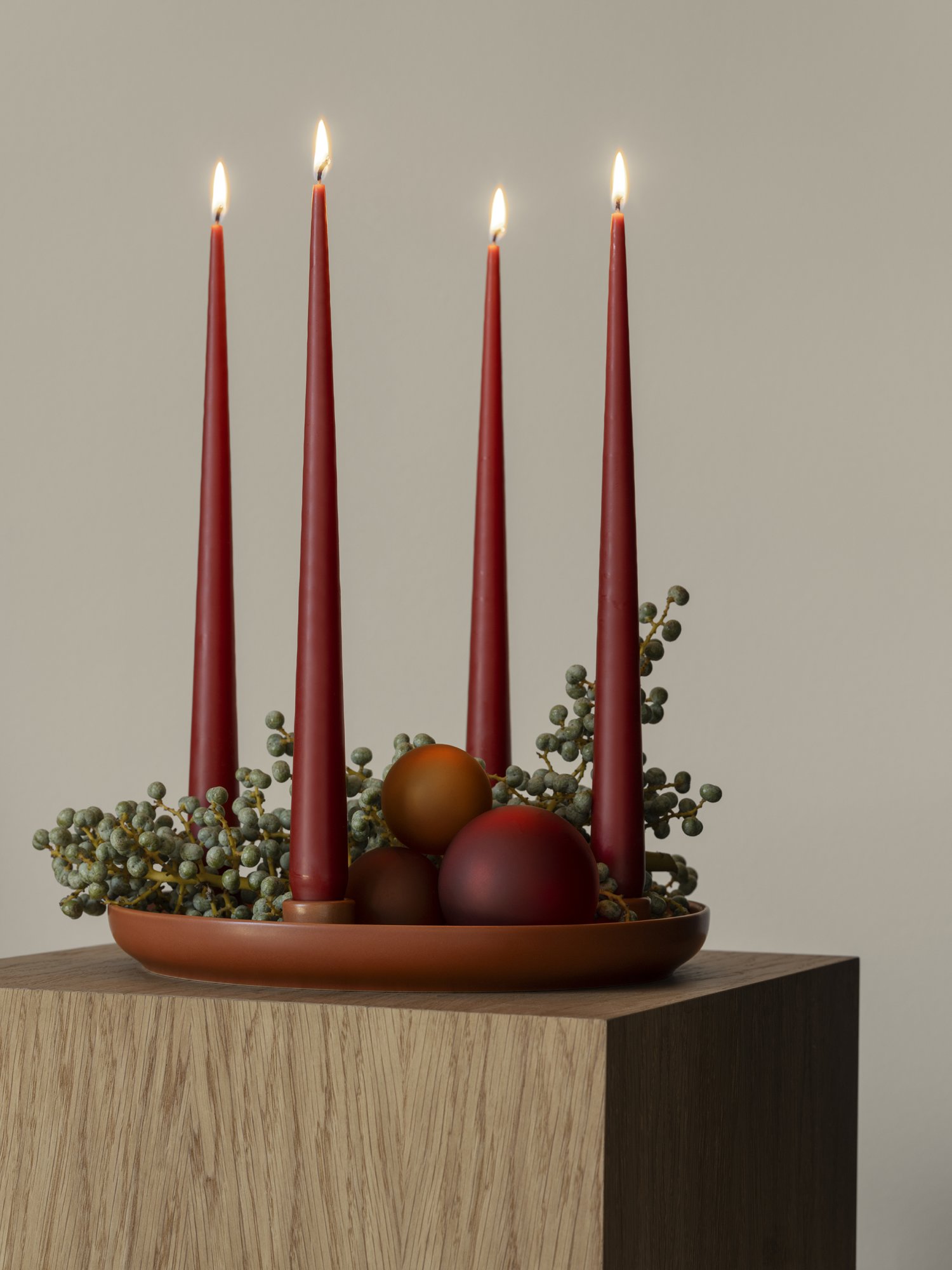 Elegant holiday centerpiece with red candles and decorative orbs on a wooden table.