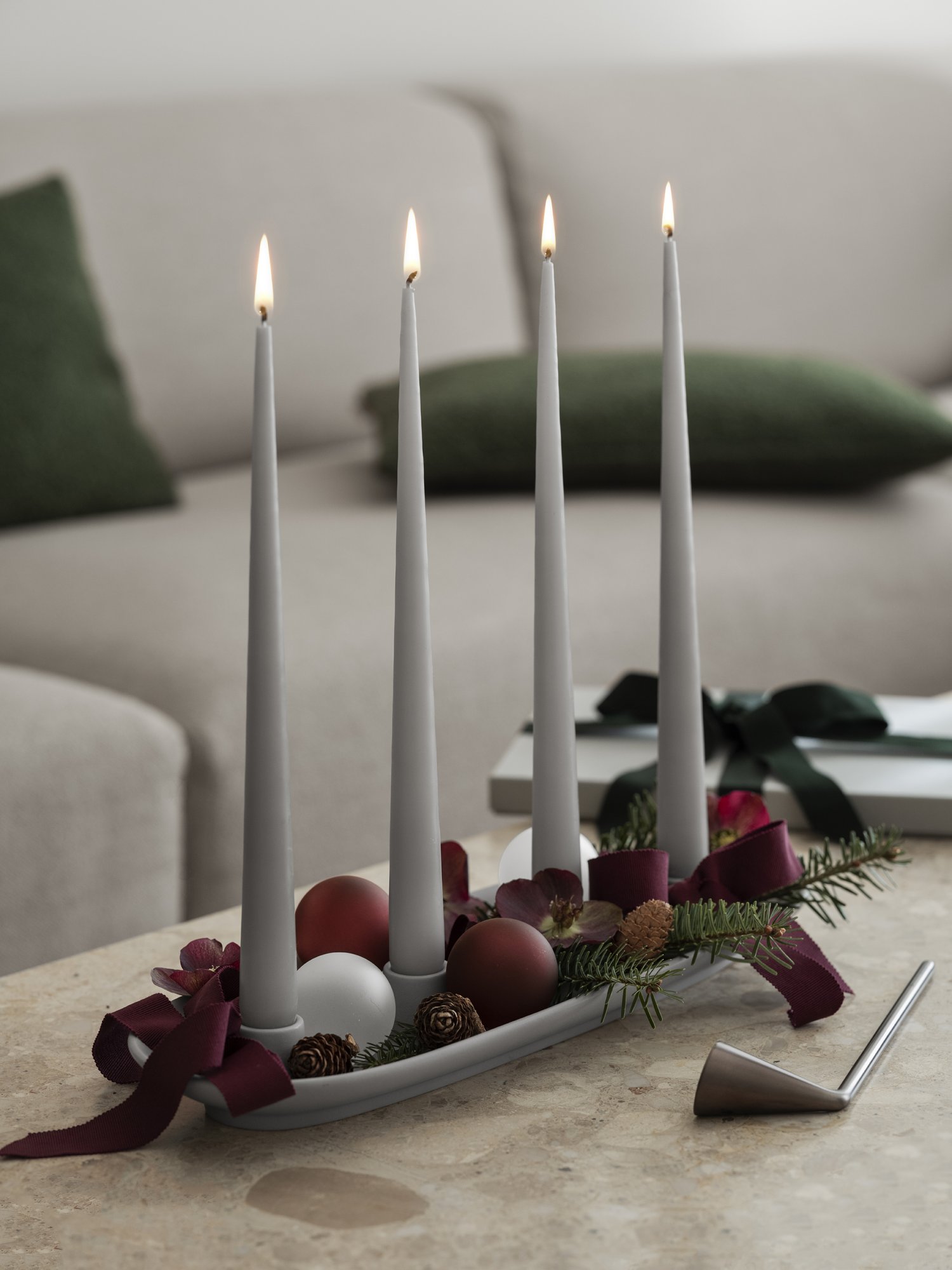 Elegant holiday centerpiece with four lit candles, decorated with ornaments and greenery.