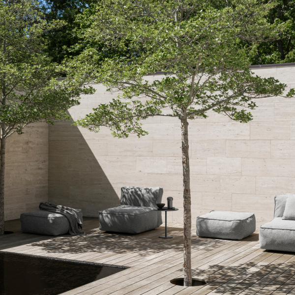 Modern outdoor lounge area with cozy seating and lush greenery by a serene water feature.