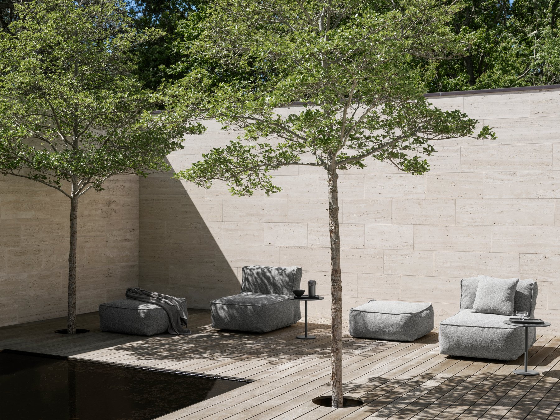 Modern outdoor lounge area with cozy seating and lush greenery by a serene water feature.