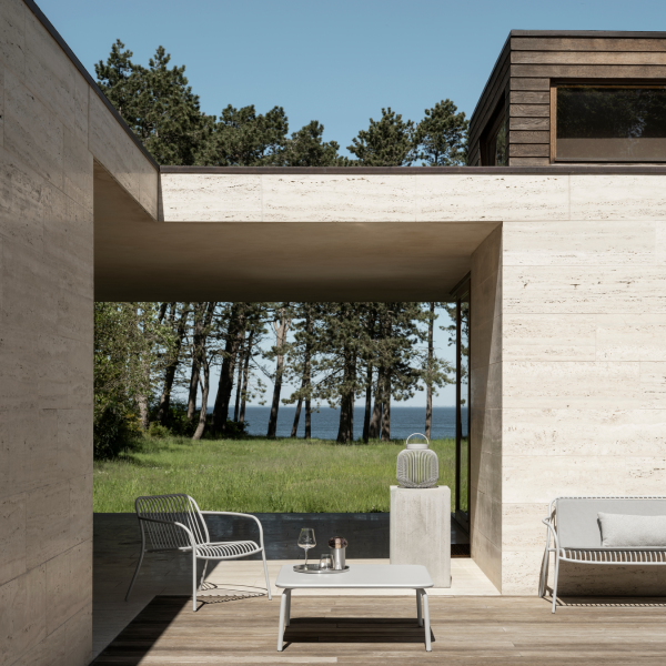 Modern outdoor living space with minimalist furniture and scenic forest view by the lake.