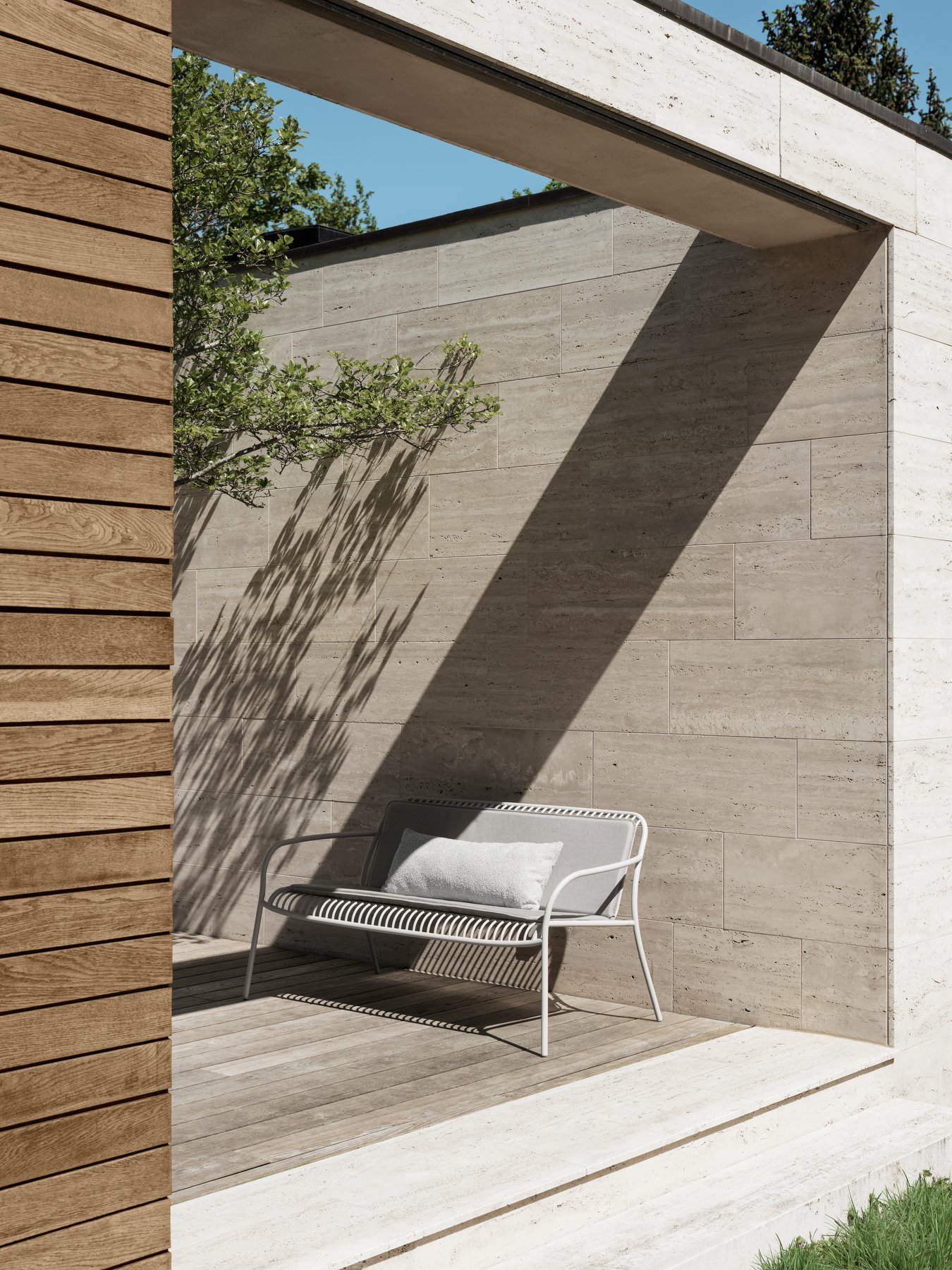 Modern outdoor seating area with natural stone wall and soft shadows from surrounding greenery.