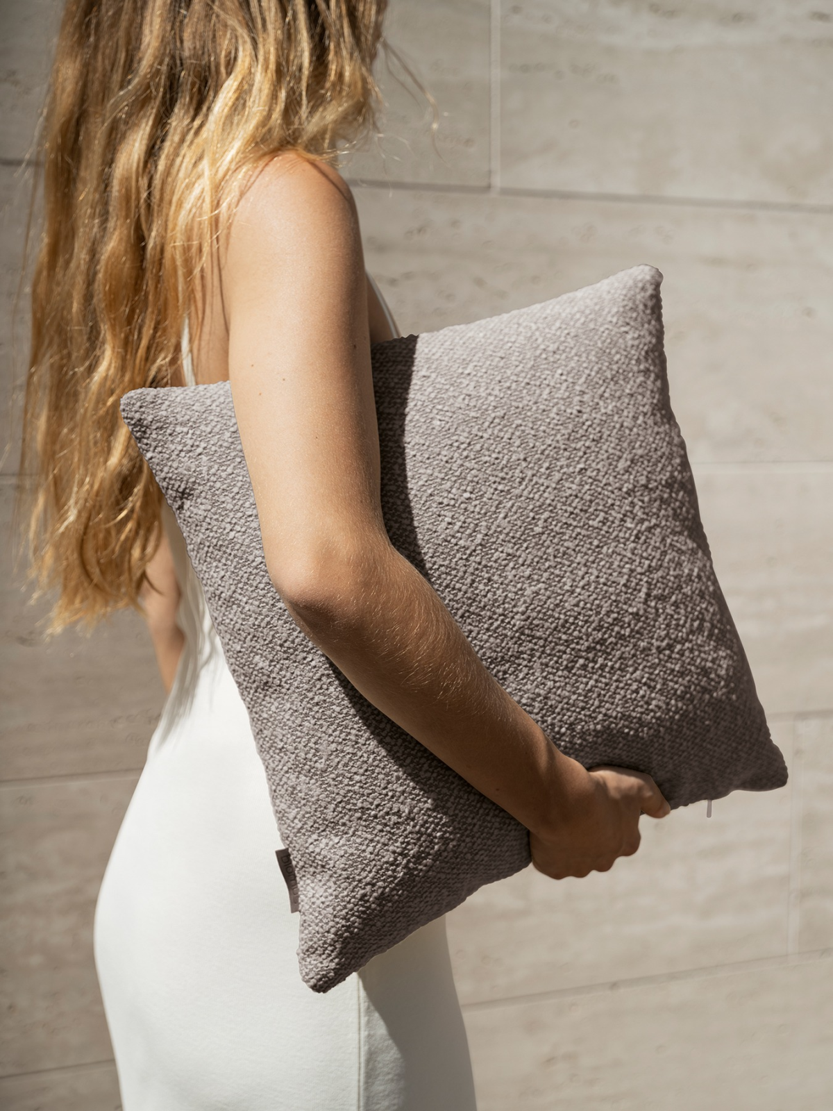 A woman holding a textured gray pillow while wearing a simple white dress.