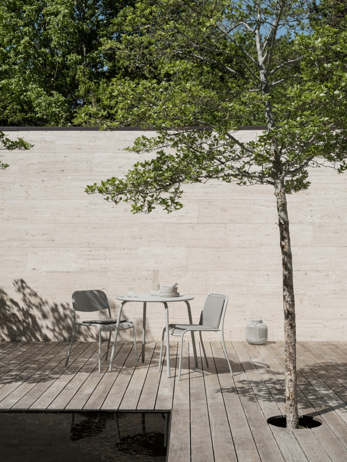 Gemütlicher Außenbereich mit Tisch, Stühlen und Baum vor einer modernen Wand.